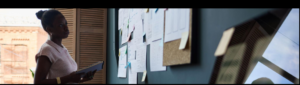 Black woman entrepreneur reviewing notes and planning systems on a wall board while reflecting on accountability, structure, and long-term execution.